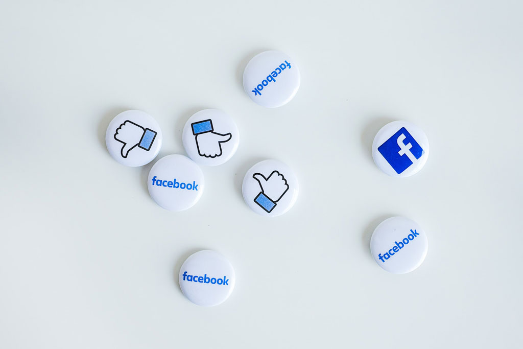 Pins with Facebook logos on them scattered on white surface.