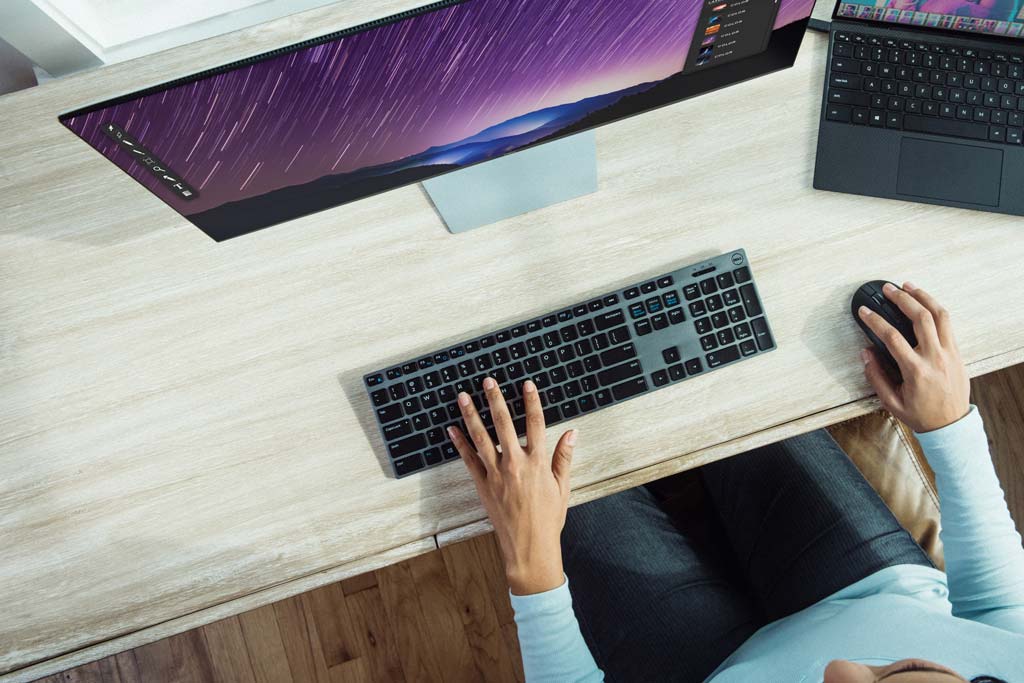 Large computer monitor, keyboard and laptop seen from above.