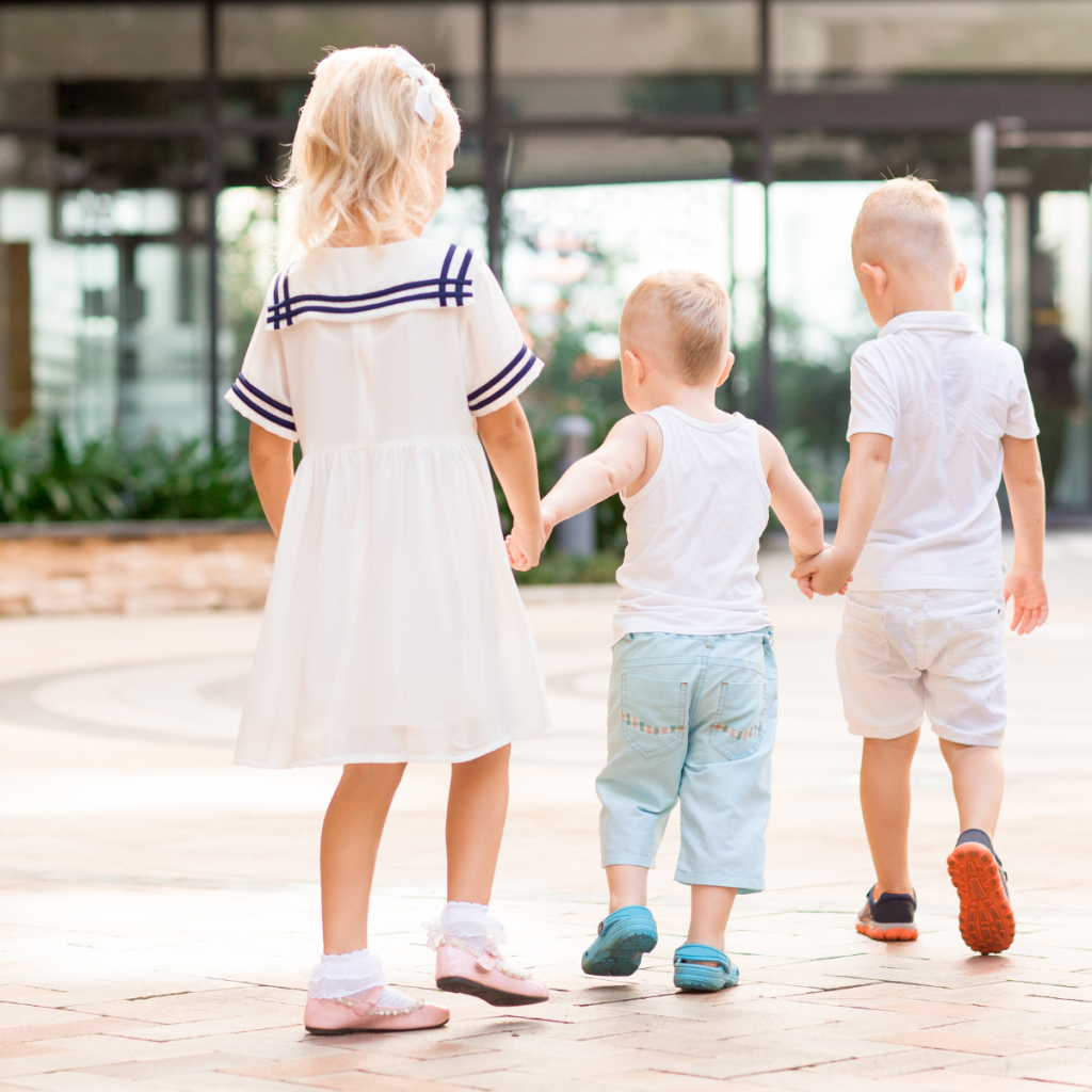 Three kids holding hands and walking outside.