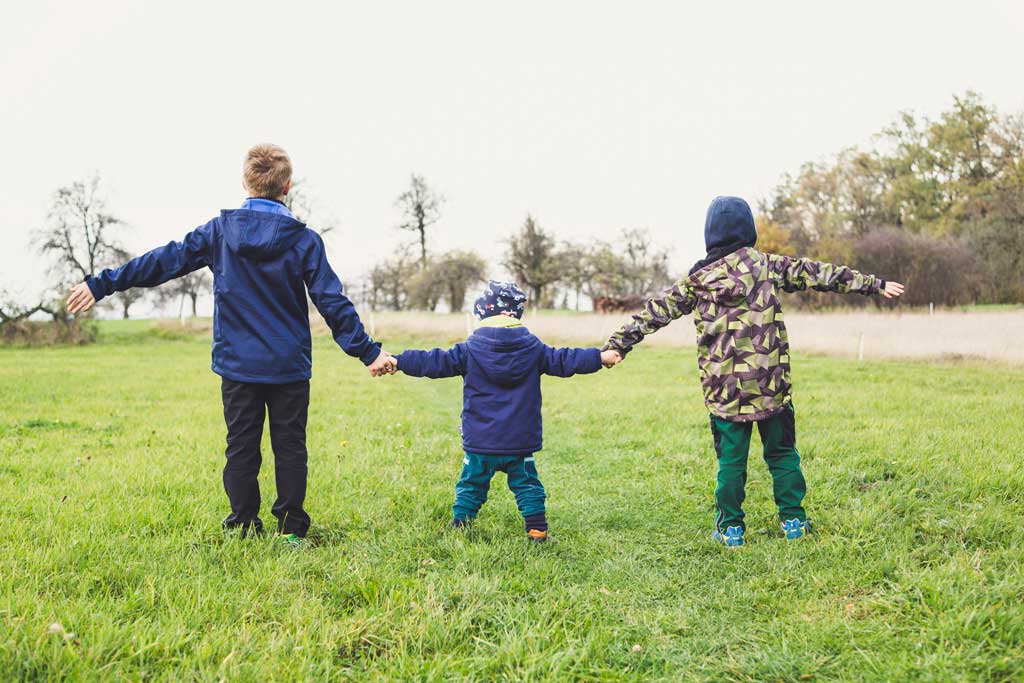 Three kids holding hands and walking outside.