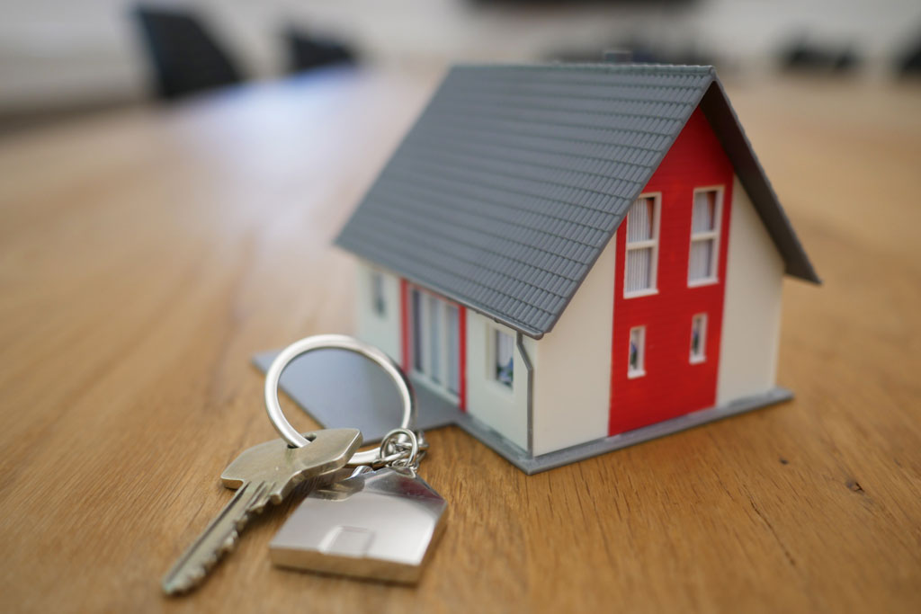 Small model home on a desktop with keys beside it.