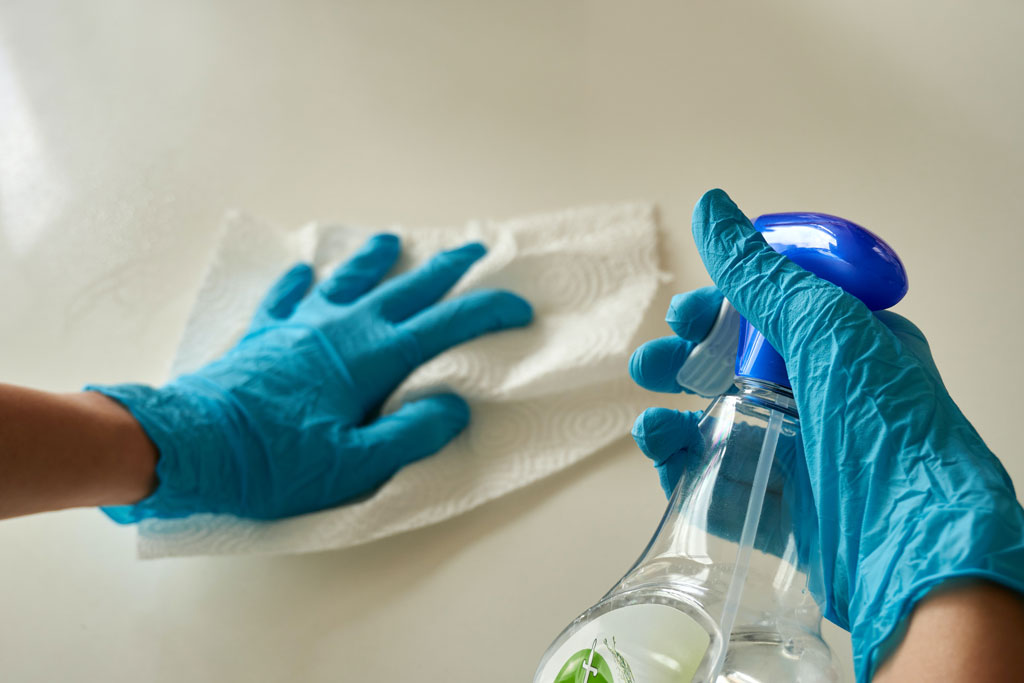 Person wearing gloves sanitizing a surface.